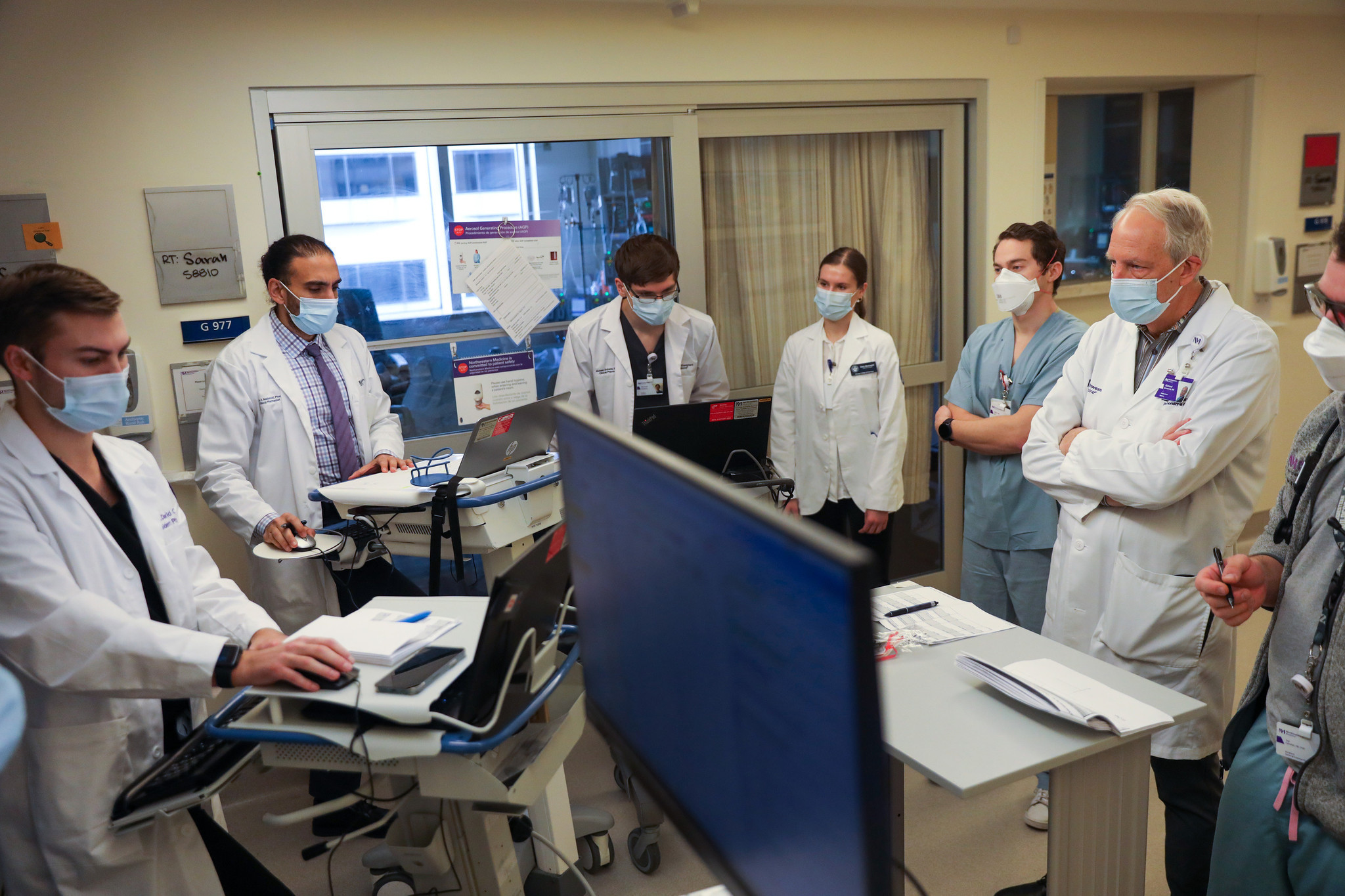 A critical care team reviewing patient monitors together during rounds in the intensive care unit
